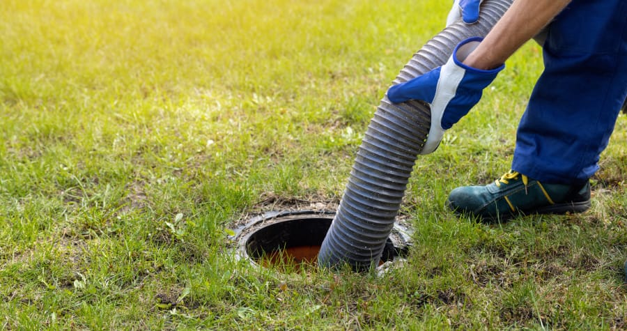 Person cleaning septic tank with hose in grass.