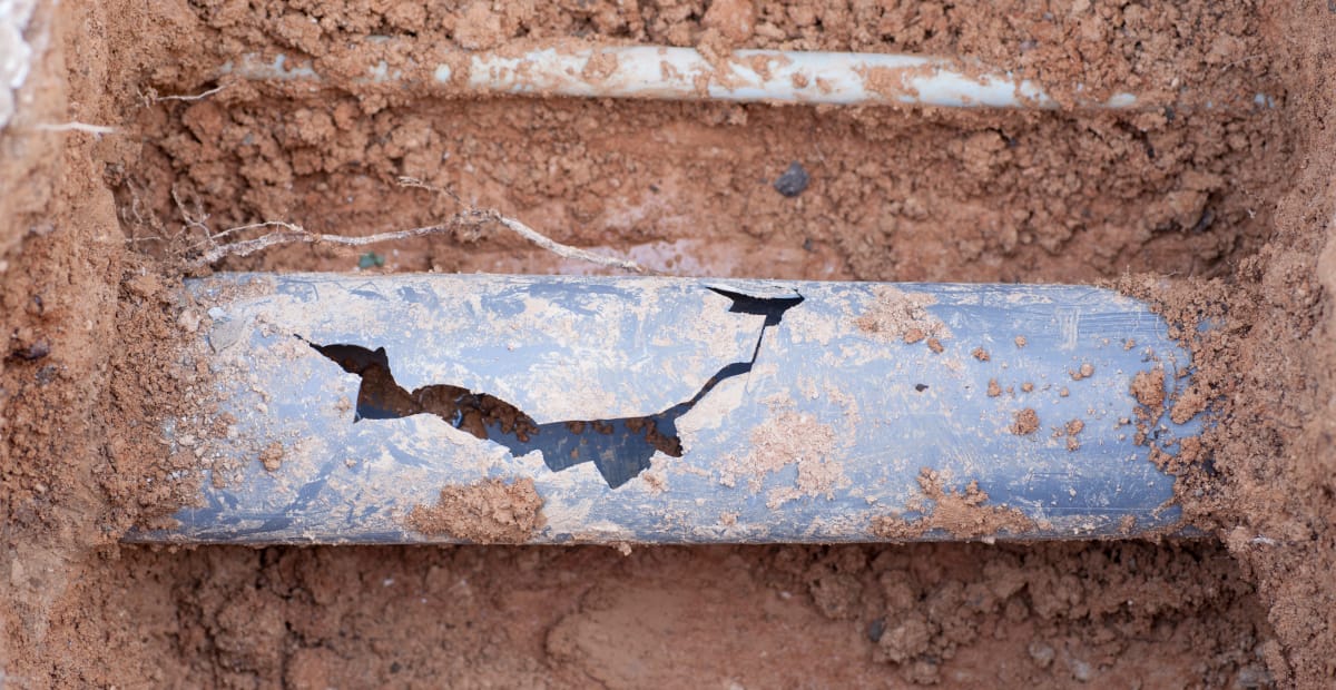 Cracked underground pipe surrounded by dirt.