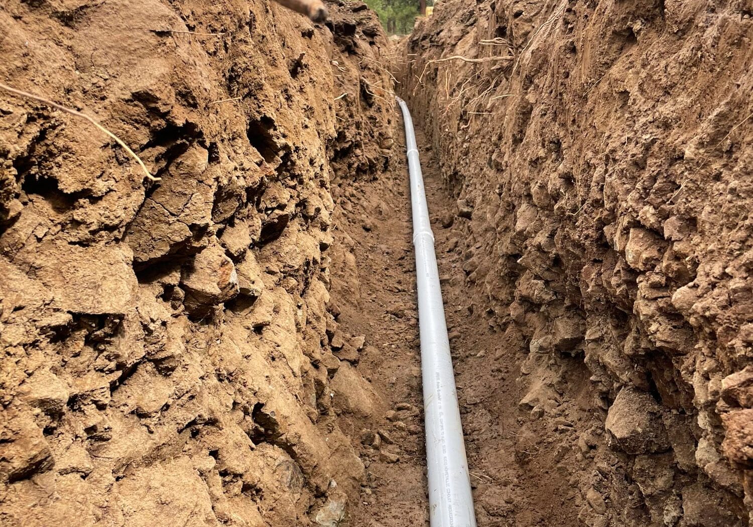 Long trench with pipe installation in forested area.